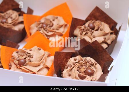 open box of chocolate cupcakes with cream top and crispy topping in paper on a white background Stock Photo