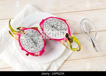 Ripe dragon fruit or pitaya cut in half in a white plate and spoon on a wooden table. Healthy vegetarian rich in B vitamins and tannin. Ready to eat. Stock Photo