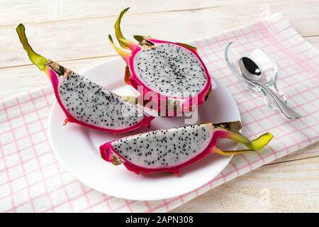 Cut into three parts ripe pitaya or dragon fruit on a plate over a white wooden table. Healthy vegetarian food rich in B vitamins and tannin. Stock Photo