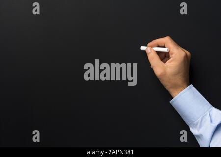 Close up of man hand holding chalk against blank black chalkboard Stock Photo