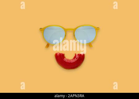 Yellow sunglasses and half bitten red donut sets as smile mouth on orange background for minimal and summer concept. Stock Photo