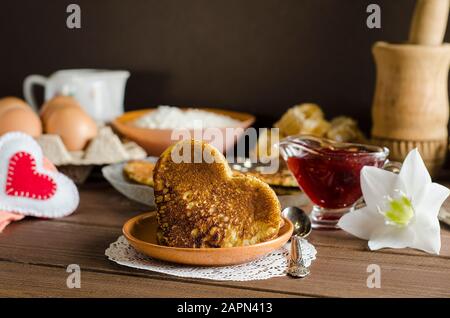 Fritters, pancakes in the form of hearts with jam and ingredients on a dark wooden background with copy space, romantic breakfast for Valentine's Day. Stock Photo