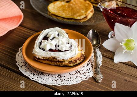 Fritters, pancakes in the form of hearts with whipped cream and jam on a dark wooden background, romantic breakfast for Valentine's Day. Mothers Day. Stock Photo