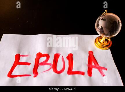 Word 'EBULA' written on a piece of white paper with a 3D globe model in a pitch-black background Stock Photo