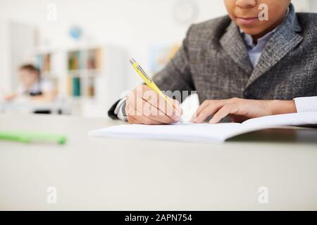 Close-up of African schoolboy sitting at the table and making notes in notebook during exam Stock Photo