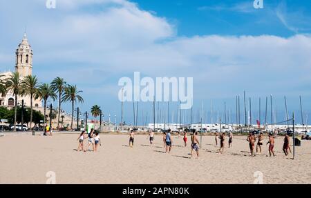 SITGES, SPAIN - JULY 27, 2018: People playing volleyball at the Platja de la Fragata beach in Sitges, Spain, highlighting the Sant Bartomeu i Santa Te Stock Photo