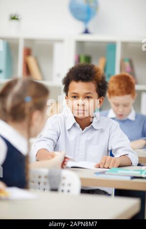 African schoolboy sitting at desk and talking to schoolgirl during a lesson in the classroom Stock Photo
