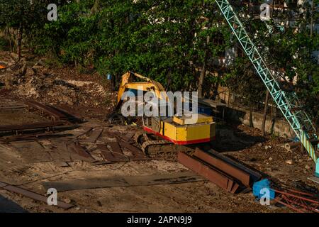 Yellow excavator on a construction site against blue sky. Heavy industry. Large tracked excavator standing on a orange ground with a palms on Stock Photo