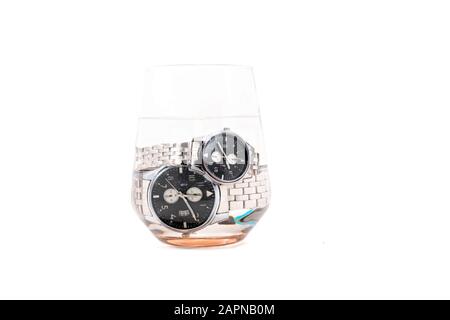 Classic black plate and silver strap round shape waterproof man and woman wristwatches dipped in glass of water isolated on white background.