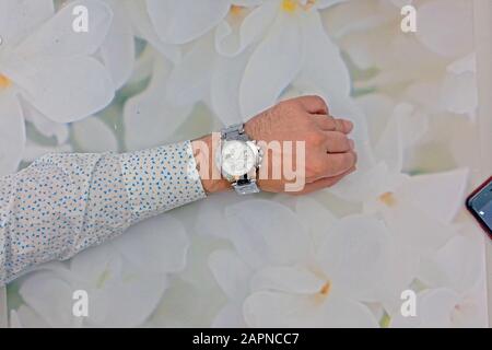 Man hand wearing silver colored classic round wristwatch white dial and timer functions on the plate. Soft flower texture in the background. Stock Photo