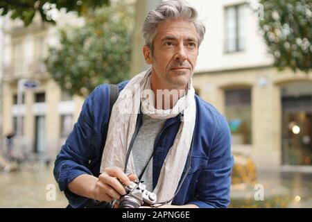 Mature photographer taking photos with vintage camera in European old town Stock Photo