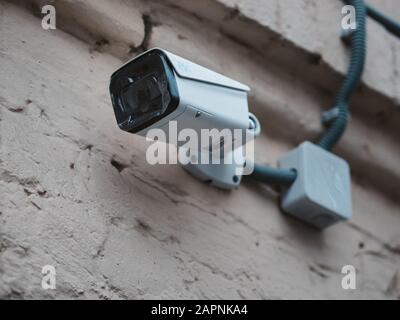 Outdoor CCTV camera mounted on the wall of an old brick house. New camera with protective films on the lens. Video surveillance on a city street. Stock Photo