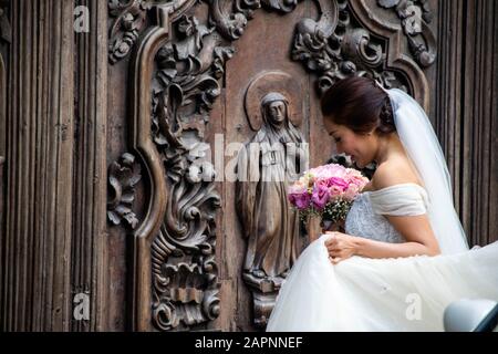 Bride in her wedding dress and veil outside the San Agustin Church in Manila, the Philippines, holding a pink flower bouquet Stock Photo