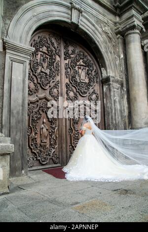 Bride in her wedding dress and veil outside the San Agustin Church, facing the old church doors, waiting for the wedding ceremony to begin Stock Photo