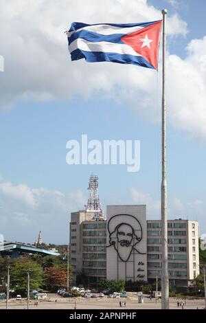 Image of Camilo Cienfuegos on the side of a building, with the Cuban flag blowing in the foreground, in Revolution Square, Havana, Cuba Stock Photo