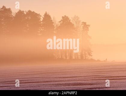 Dramatic foggy sunset landscape on frozen winter lake in Finland. Stock Photo