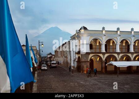 Street scene of Avenida Sur with Volcan de Agua in the background. Backpackers crossing Plaza Mayor (Parque Central), Antigua, Guatemala Stock Photo
