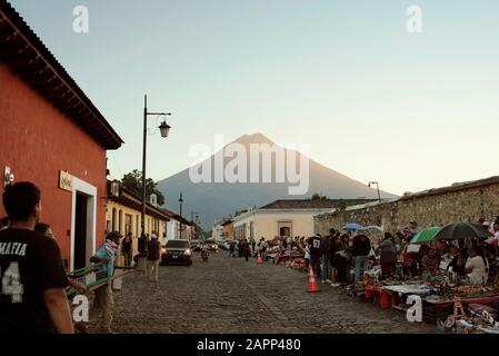 Busy street view of local artisan market and Volcan de Agua in the background. Iglesia del Carmen, Antigua, Guatemala. Jan 2019 Stock Photo