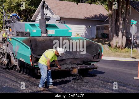 The worker uses a shovel to spread hot asphalt on the road of the bitumen laying machine. Road construction. Stock Photo