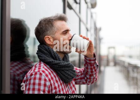 Young man leaning against a wall drinking from a reusable cup Stock Photo