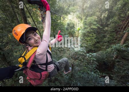 Woman Tourist Wearing Casual Clothing On Zip Line Or Canopy Experience In Laos Rainforest, Asia Stock Photo