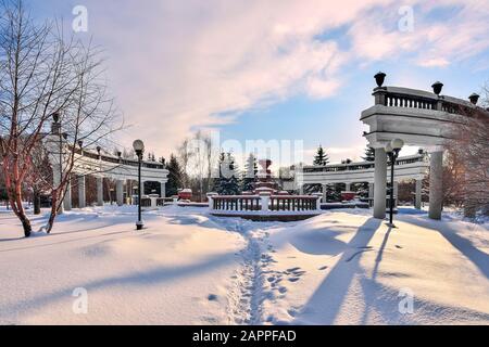 Winter walk through the snow-covered city park between snowdrifts to the fontain - a beautiful winter cityscape. Narrow path in deep fresh snow after Stock Photo