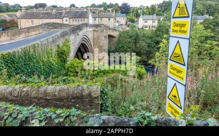 Bridge over the River Tees and a signpost re the dangers of deep water, strong currents and a weir. Barnard Castle, County Durham, England, UK. Stock Photo