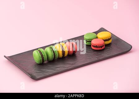 Tasty french macarons in a black serving plate on pink pastel background. Red, yellow and green macarons Stock Photo