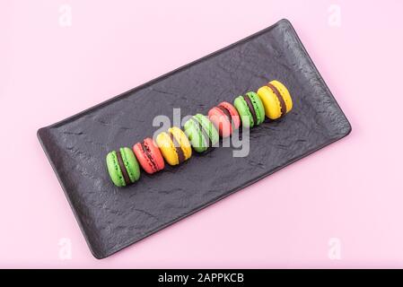 Top View of Tasty french macarons in a black serving plate on pink pastel background. Red, yellow and green macarons Stock Photo