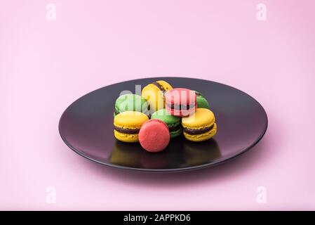 Tasty french macarons in a black plate on pink pastel background. Red, yellow and green macarons Stock Photo