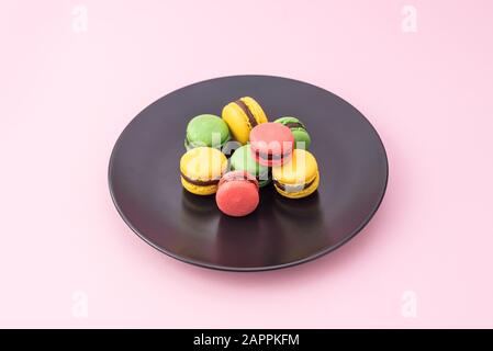 Tasty french macarons in a black plate on pink pastel background. Red, yellow and green macarons Stock Photo