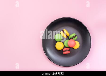 Top View of Tasty french macarons in a black plate on pink pastel background. Red, yellow and green macarons Stock Photo