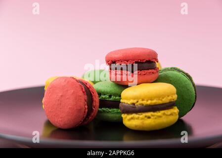 Close Up View of Tasty french macarons in a black plate on pink pastel background. Red, yellow and green macarons Stock Photo