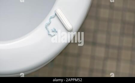 Tampon lies on the toilet bowl. High angle view with soft focus. Stock Photo