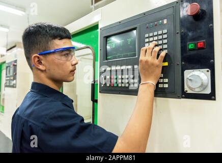 CNC operator, mechanical technician worker at metal machining milling center in tool workshop inserting data with keyboard wearing Stock Photo