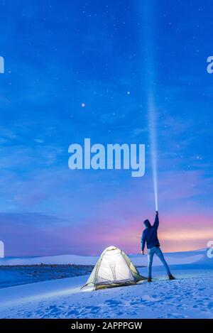 Man by tent shining torch into sky, White Sands National Monument, New Mexico, US Stock Photo