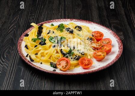 Tagliatelle with tomato, parmesan, chopped olives and basil Stock Photo