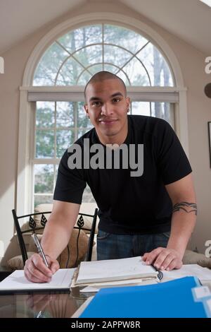 Male college student at home making notes in a notebook for homework Stock Photo