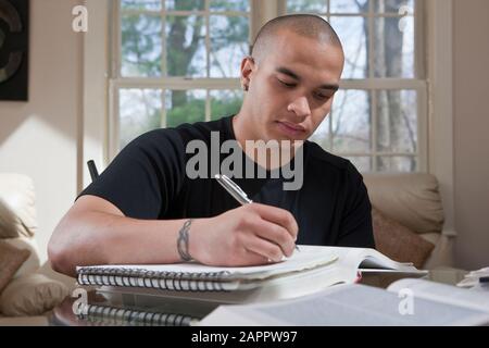 Male college student sitting at home making notes in a notebook for homework Stock Photo