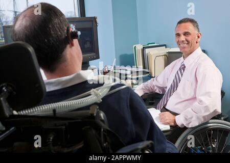 Businessmen in wheelchairs working in an office together Stock Photo