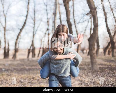 Happy young joyful couple having fun piggybacking laughing together in the autumn Stock Photo