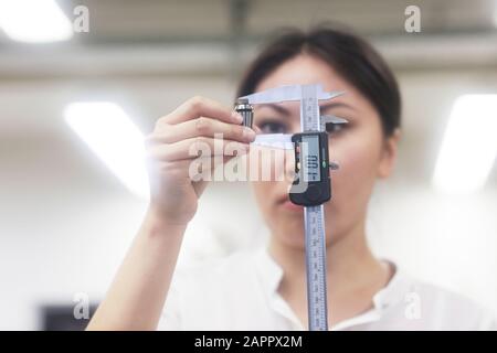 Asian woman measuring piece of gadget in office Stock Photo