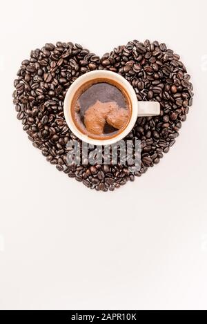 Top view of tasty coffee in cup or mug with heart made of coffee grains on white background Stock Photo