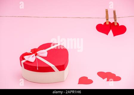 Heart shaped gift box and red paper hearts on pink pastel background. Clothes pegs and red paper hearts on rope. Valentines day concept Stock Photo