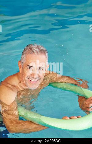 Senior man doing aqua fitness in the swimming pool with a swimming board Stock Photo