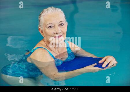 Smiling senior woman makes aqua fitness with swimming board in the swimming pool Stock Photo