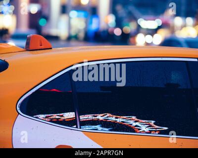 Yellow taxi car with reflections of LED advertising in tinted windows. Multi-colored festive lights in bokeh on background. New Year or Christmas deco Stock Photo