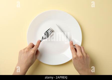 Female hands hold fork and knife on beige background with plate, top view Stock Photo