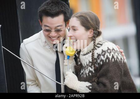 Young woman talking on a pay phone and her friend standing beside her Stock Photo