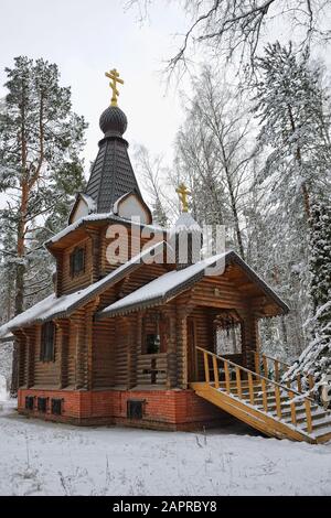 = Snow-Covered Boris and Gleb Chapel in the Pine Woods =  Front angle view of the snow-covered wooden chapel in a pine grove near the village of Buzae Stock Photo